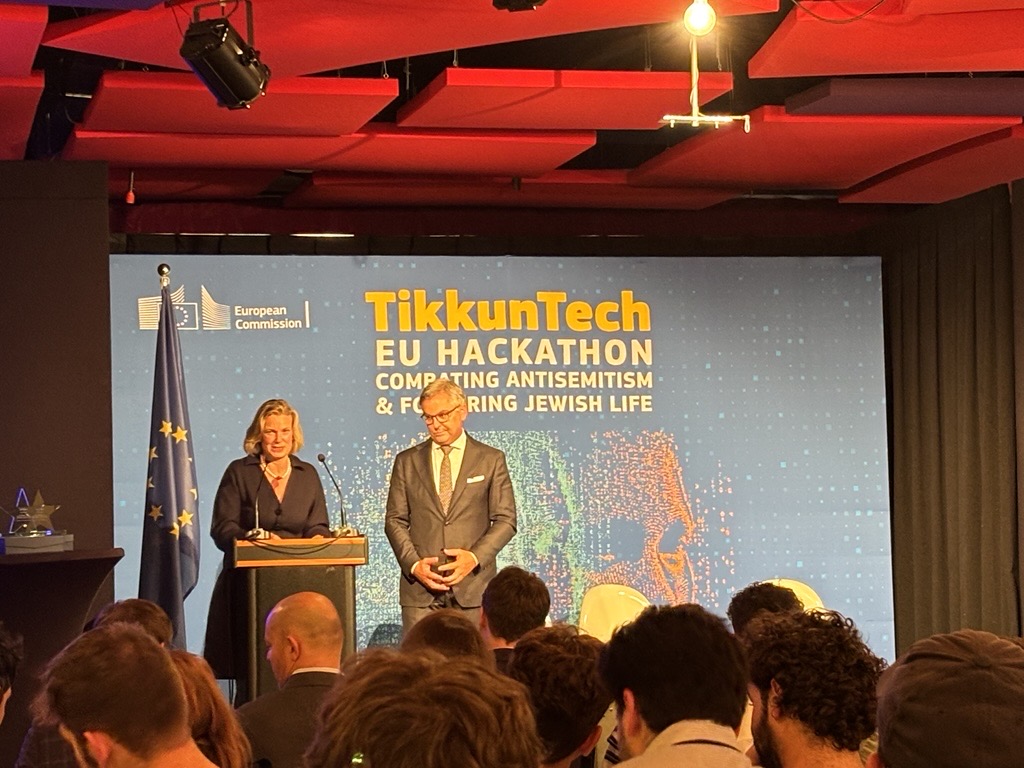 Zwei Redner vor einer Bühne beim TikkunTech EU Hackathon der Europäischen Kommission zu Antisemitismus und jüdischem Leben